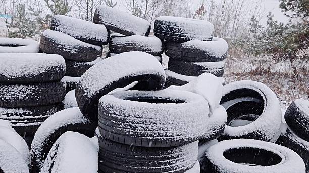 Stacking used car tires covered with fresh snow outdoors. Piles of old automobile tires accumulating snow in winter storage yard during snowfall