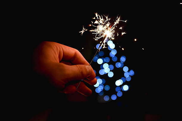 Hand holding a burning sparkler with festive blue bokeh lights in the dark background