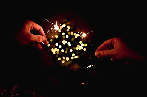 Hands holding two illuminated sparklers against a background of festive bokeh lights during a celebration