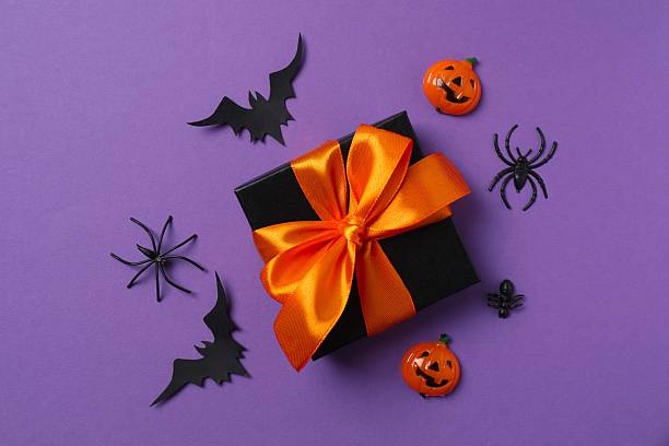 istock Halloween poscard with festive gift box and decorations on orange background . Top view, space for text 2253842258