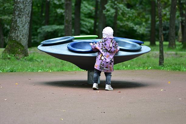Toddler playing with a round playground carousel in a park. Child exploring movement and balance through active outdoor play, developing coordination and curiosity in a natural green environment.