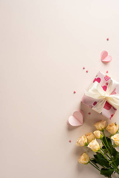 istock A soft vertical pink background hosts a gift box wrapped with hearts and a pale ribbon, alongside creamy roses. Valentine romance and gift display suitable for greetings and celebration 2253853699