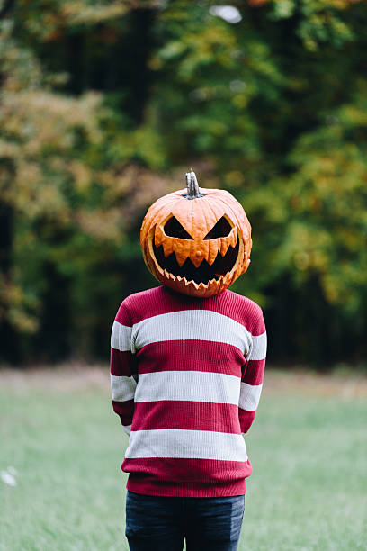 istock Person Wearing a Pumpkin Head Standing Outdoors in Autumn 2253855321