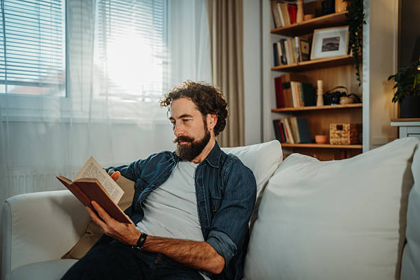 istock Man relaxing on sofa reading book at home 2253856364