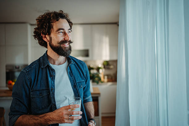 istock Smiling man drinking water looking out window in kitchen 2253856391