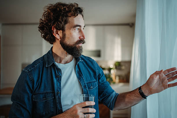 istock Man looking out window holding drink at home 2253856412