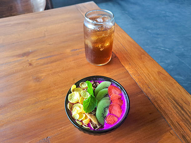 Dragon Smoothie Bowl with dragon fruit, banana, strawberry cornflakes cereal, granola, fresh milk and kiwi. Fresh tea Iced in glass. Food And Drink Menu.