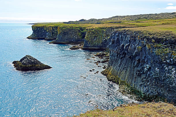 Dramatic cliffs rise along the Snaefellsnes Peninsula in Iceland, overlooking the Atlantic Ocean. The rugged coastline showcases striking rock formations and green vegetation, highlighting the raw natural beauty and striking landscapes of Iceland’s western coast.