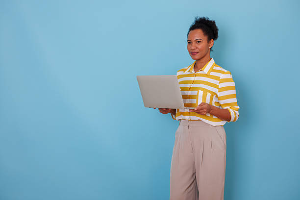 istock Woman working on laptop, presenting information, standing against blue background with copy space 2253863772