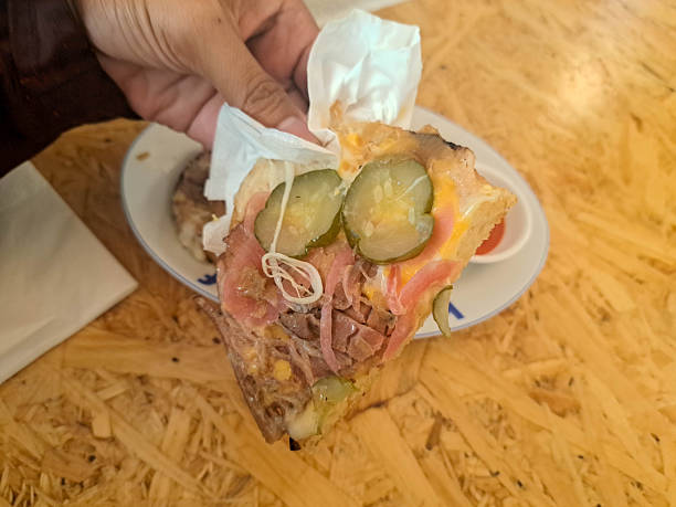 A young man is eating Sourdough Sandwich Corned Beef with bread, cheese, honey mustard, pickle cucumber, pickle onion and caramelized onion. Food Menu.