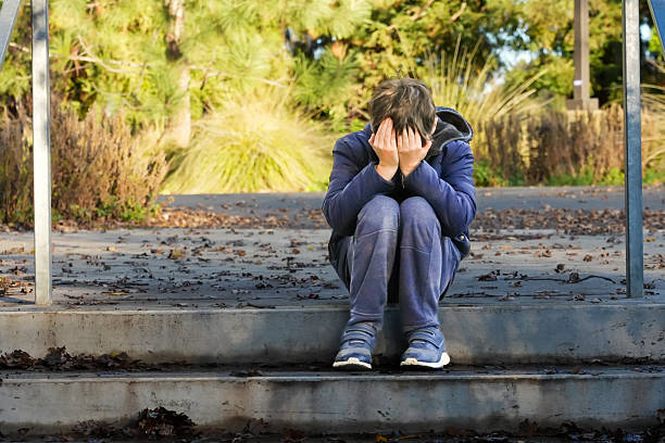 Crestfallen Crying child boy sitting at a park steps covering his face