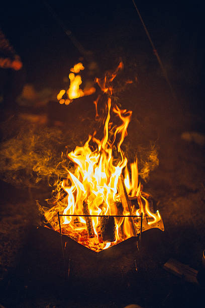A bright campfire burning intensely in the dark night outdoors. Tall flames and glowing firewood create a dramatic and powerful atmosphere, symbolizing warmth, energy, survival, resilience, and human connection with fire.