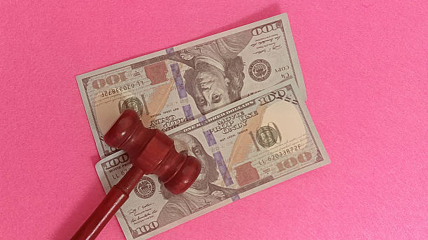 istock Judge gavel on hundred dollar bills with pink background 2253879012
