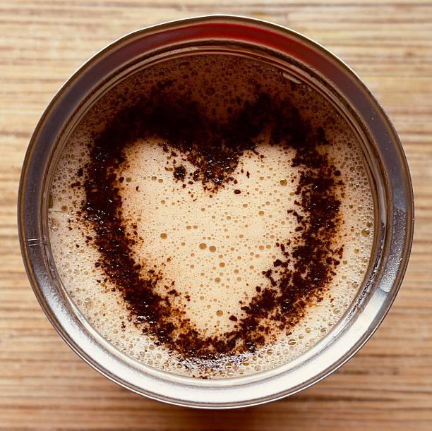 A close-up view of a cup of coffee with a heart-shaped pattern formed by coffee grounds on the surface