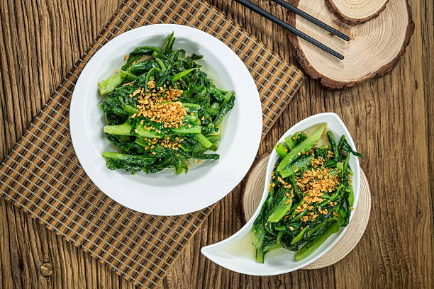 Two plates of vibrant green leafy vegetables topped with minced garlic served on a wooden table with chopsticks.