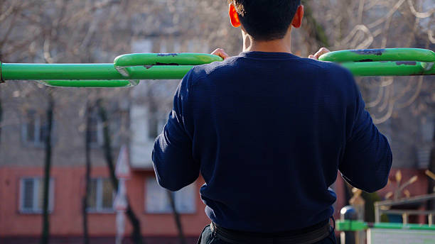 istock Back view of man doing pull-ups on horizontal bar outdoors. 2253885468