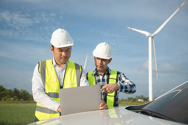 istock Renewable energy maintenance. Engineer using laptop computer checking system of wind turbine at windmill field farm station. Wind turbine energy storage system. Workers meeting to check around the area 2253887186