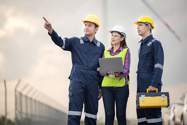istock Renewable energy maintenance. Engineer using laptop computer checking system of wind turbine at windmill field farm station. Wind turbine energy storage system. Workers meeting to check around the area 2253887217