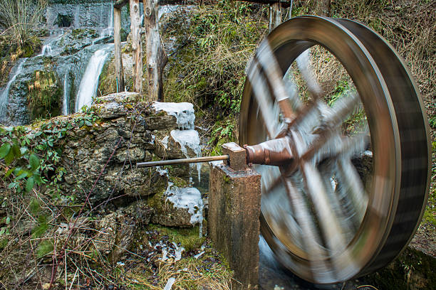 A picturesque frozen water mill surrounded by serene winter nature, featuring icy textures, snow-covered trees, and a tranquil river partially frozen under a crisp blue sky. Perfect for themes of winter landscapes, rustic architecture, and seasonal beauty.