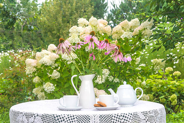 Two white cups of tea, tea pot, bouquet of pink flowers on a table in a blooming garden