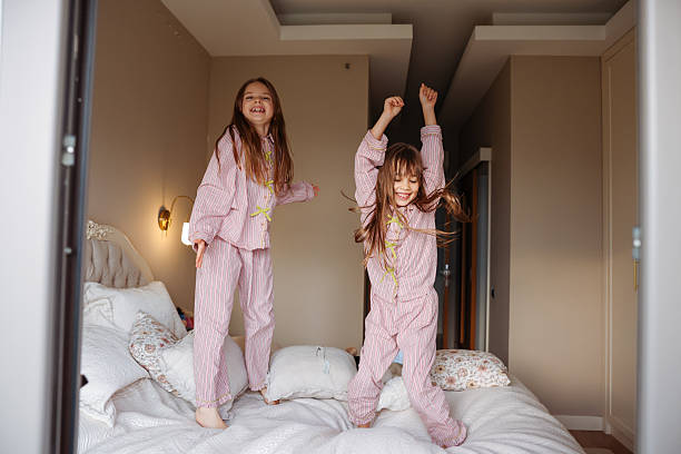 istock Two young sisters are jumping on a bed, having fun and enjoying their time together. 2253901955