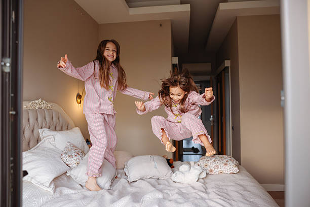 istock Two young sisters are jumping on a bed, having fun and enjoying their time together. 2253902183