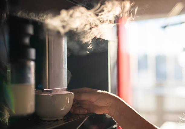 Human hand is making hot coffee with steam from machine.