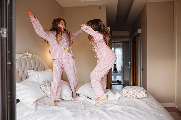 istock Two young sisters are jumping on a bed, having fun and enjoying their time together. 2253902265