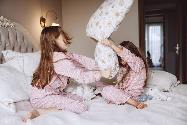 istock Two sisters are having a playful pillow fight on a bed, laughing and having a great time. 2253902514