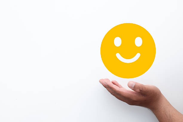 Hand holding yellow smiley face icon on white background. Concept of customer satisfaction survey, happy feedback review, good mental health, positive emotion, and excellent service rating.