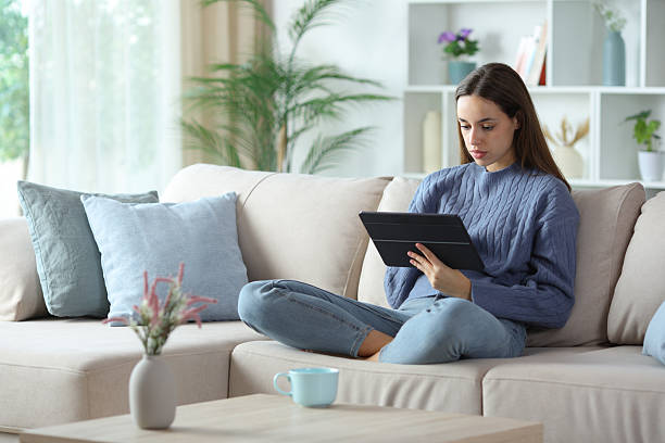 istock Serious woman in blue using digital tablet on a sofa 2253907806