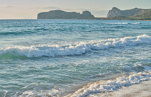 Photo from the island of Crete (Greece): A tranquil Greek seascape with turquoise waves rolling onto a sandy shore, distant rugged cliffs, and a calm, sunlit horizon that evokes peace and natural beauty of Greece.