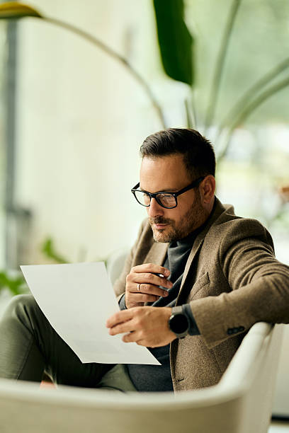 istock Professional Man Reading Document in Modern Office, Glasses On, Focused, Business Style 2253913764