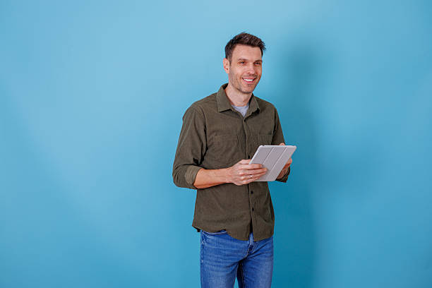 istock Smiling man holding a digital tablet against a blue background, using technology for communication and online business 2253913997