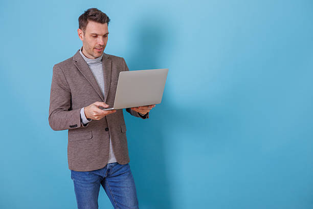 istock Professional man standing, working on laptop, researching information, creating content on blue background 2253916431