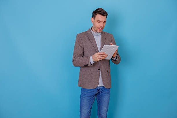 istock Mid adult man using digital tablet against blue background, working with modern technology 2253916800