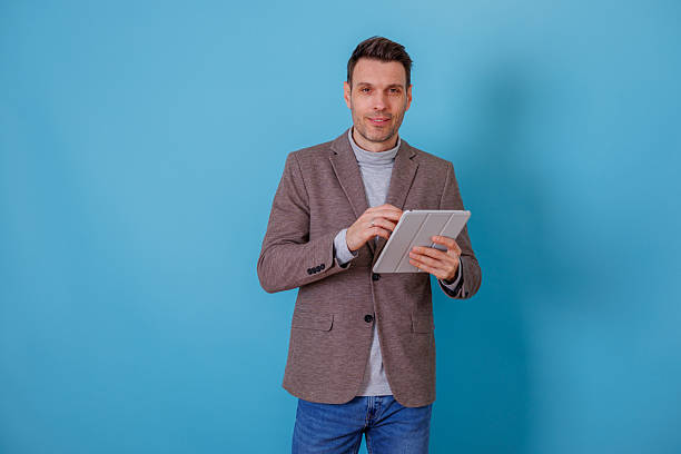 istock Young adult man in smart casual attire holding a tablet, using modern technology for communication and online business 2253916804