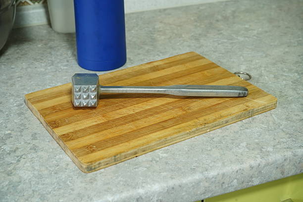 Iron meat mallet lies on a kitchen wooden board. Kitchen table background
