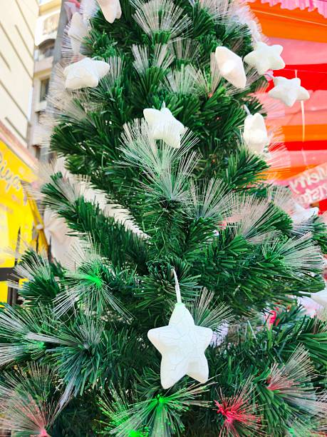 Closeup of white decorative ornaments hanging on green Christmas tree branches with festive lights. Concept of holiday decoration, winter celebration, seasonal tradition, festive atmosphere, home decor, joyful occasion.