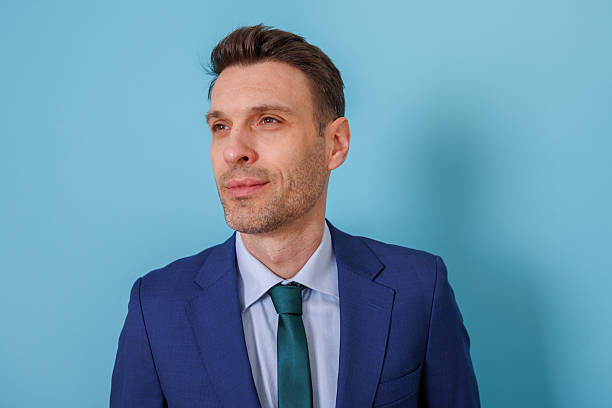 istock Businessman looking away with confident expression, wearing blue suit and tie on blue background 2253918732