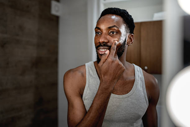 istock Black man applying face cream while looking in a bathroom mirror with lights, focused and confident during a morning skincare routine at home, expressing self care and modern lifestyle 2253921916