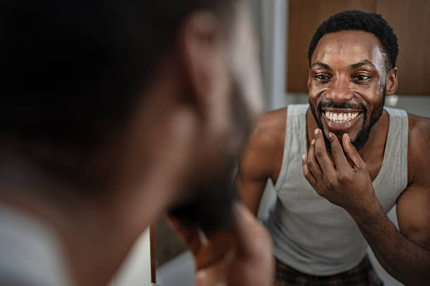 istock Cheerful Black man smiling at his reflection while touching his beard in the bathroom mirror. Relaxed home grooming moment, natural light, confidence and everyday self-care lifestyle 2253921940