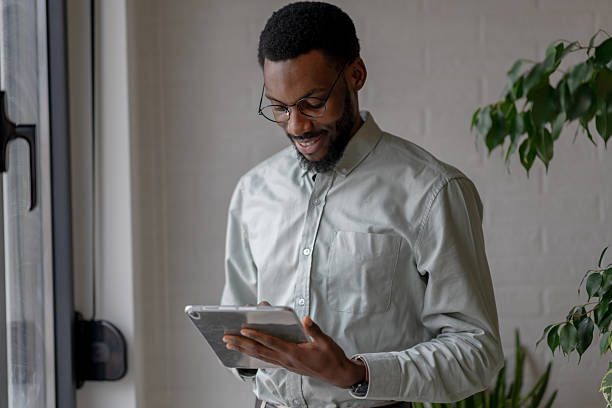 istock Thoughtful Black professional man wearing glasses, using a digital tablet in a bright modern office, focused and reflective, expressing concentration, decision making, and calm confidence 2253923307