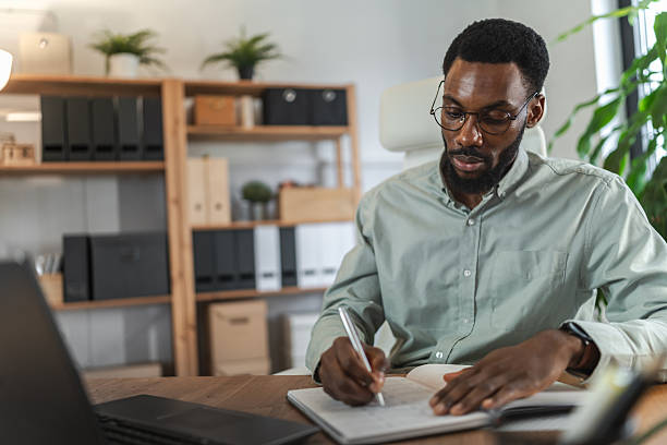 istock Young African American man working from home, writing notes at a desk with a laptop in a modern home office, focused on planning, productivity, and remote business work 2253923714