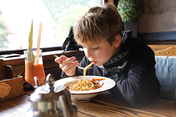 istock Boy eating noodles with fork in restaurant 2253924951