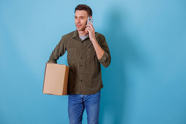 istock Man holding cardboard box talking on smartphone, managing package delivery and logistic services 2253929490