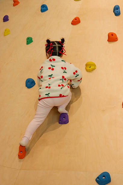 A toddler climbing a colorful indoor play wall, developing balance, strength, and coordination through active play. Concept of early childhood physical development and safe indoor activities.