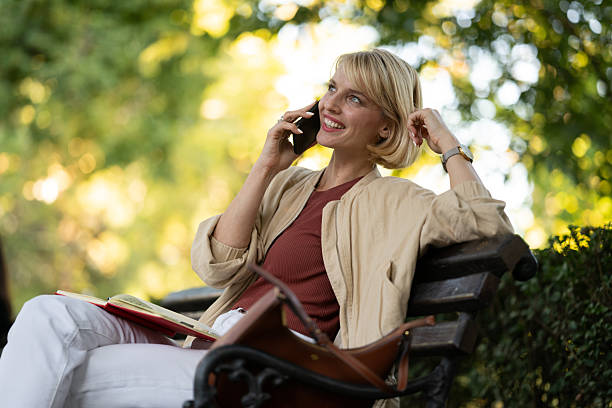 istock Woman talking on phone while sitting on bench in park surrounded by green trees during daytime 2253930788
