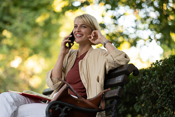 istock Woman talking on phone while sitting on a bench in a park during daytime 2253931968