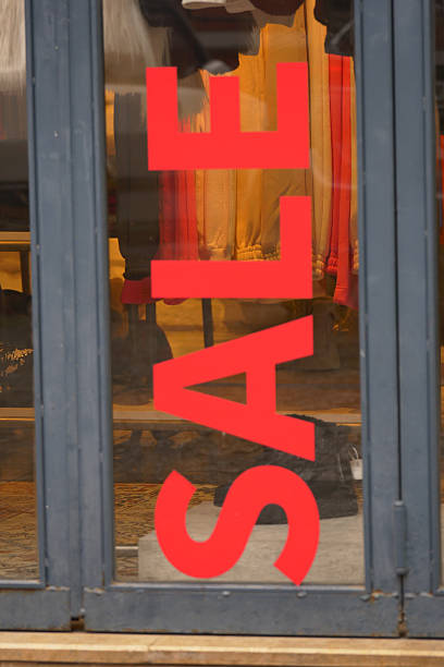 Bright red sale sign draws attention to shop window during daylight.